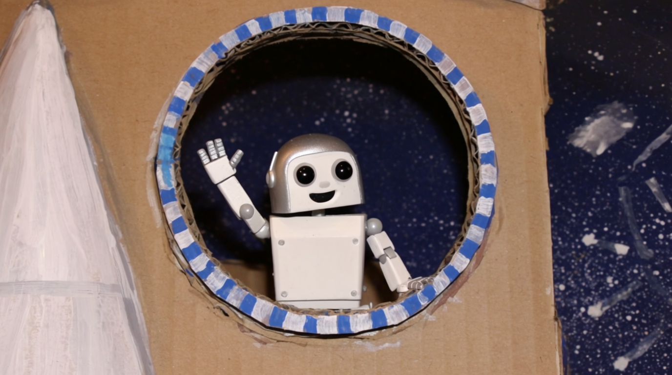 段ボールの宇宙船から手を振るおもちゃのロボット